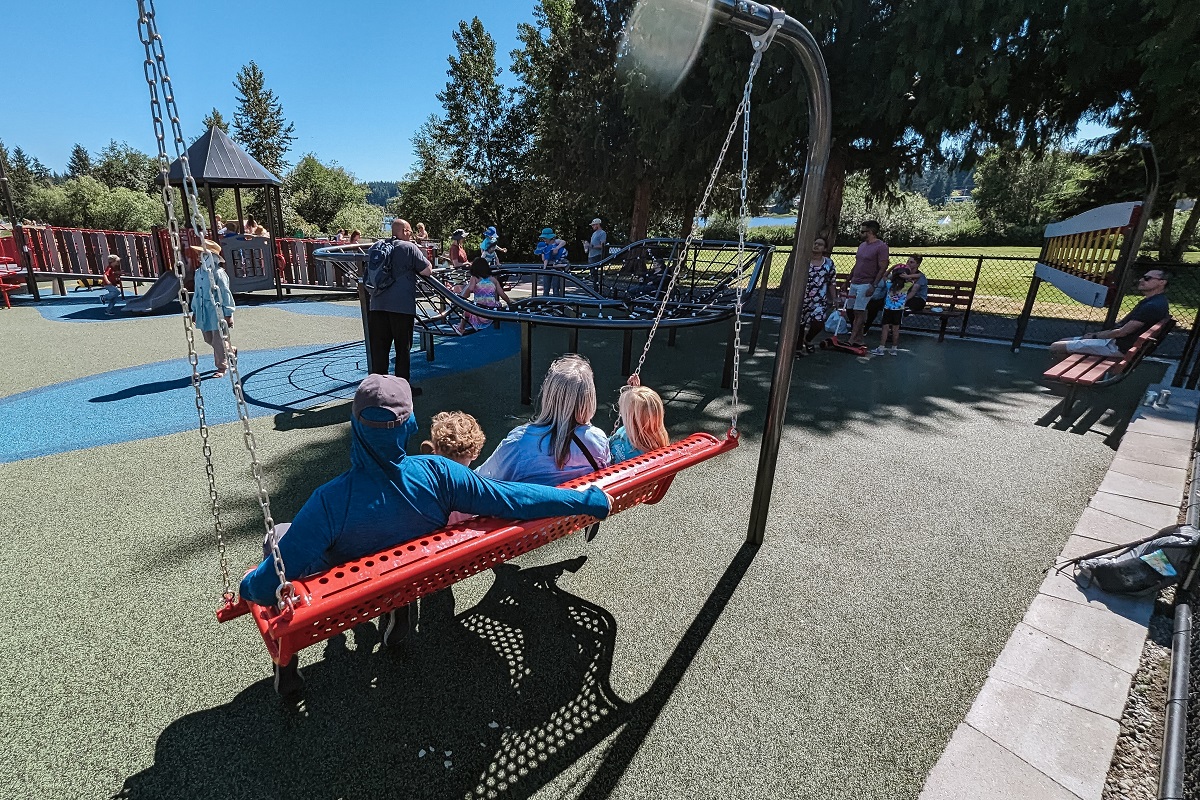 Family relaxes on a porch-style group swing at the new Hazel Miller playground at Ballinger Park in Mountlake Terrace near Seattle