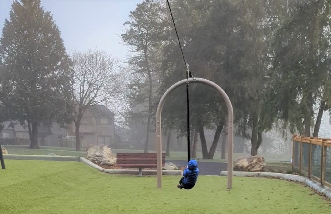 Young child in blue jacket riding zipline at new Westside Park playlground in Redmond