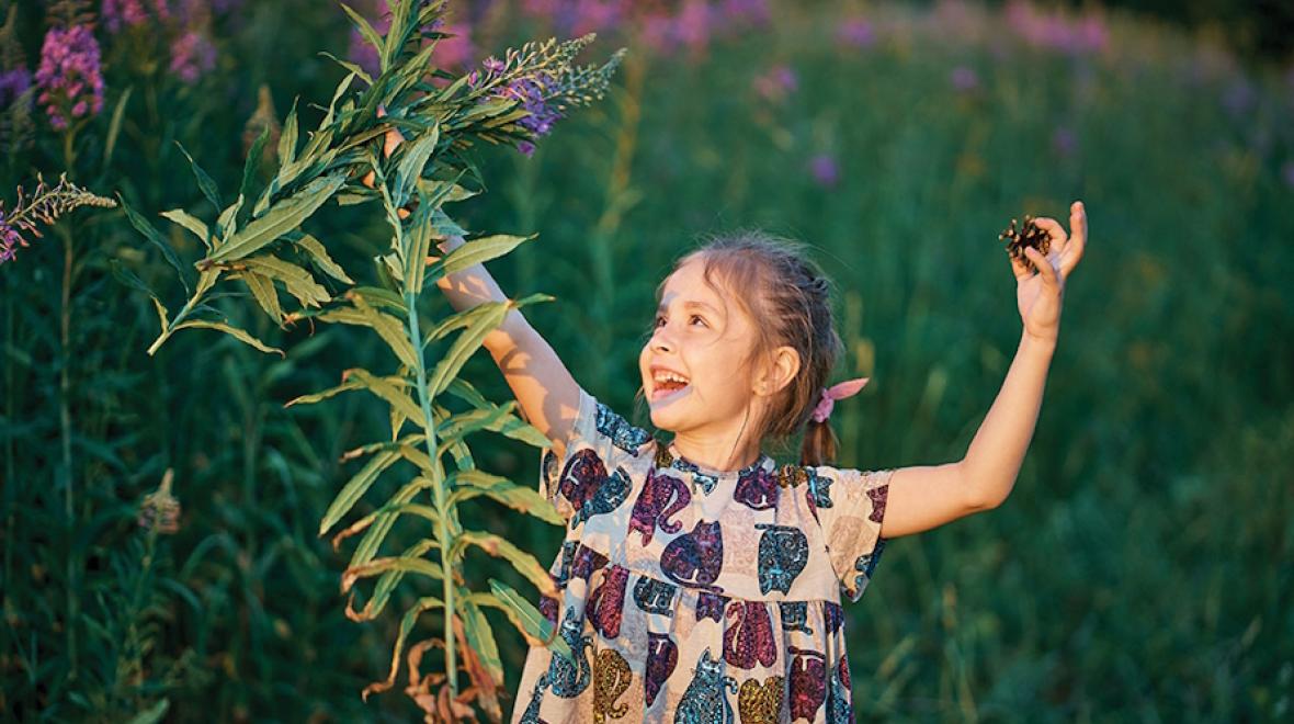 Young girl holding flowers in one hand and a pine cone in the other, looking happy in the sunshine 