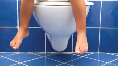 Child feet over the edge of a toilet potty training regression