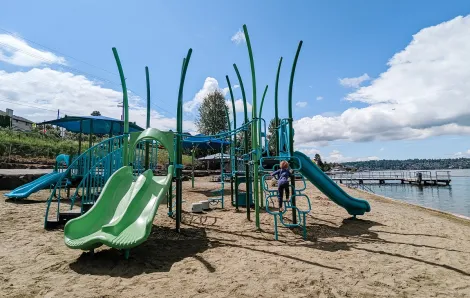 Child climbing on a blue and green play structure on the sand near the water