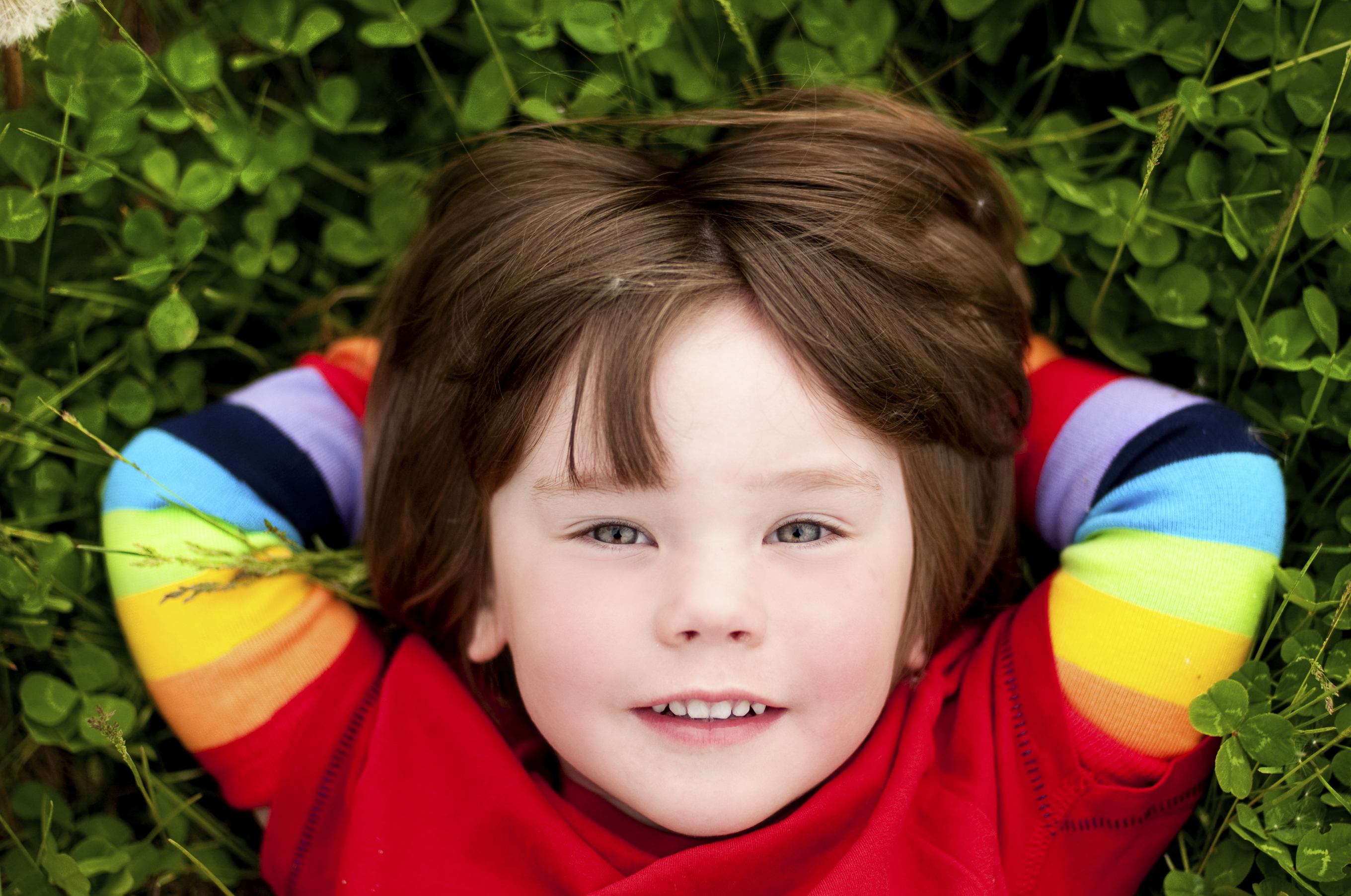 Small child in the grass wearing rainbow sleeves