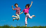 Kids jumping on grass with blue sky.