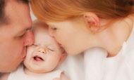 Mom and dad kissing newborn baby