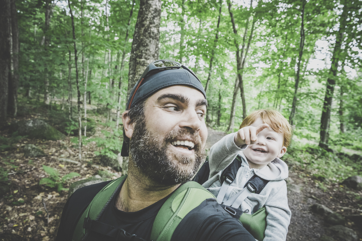 A close up of a dad carrying a baby in a hiking backpack they are smiling in the woods happy camping with babies and toddlers tips