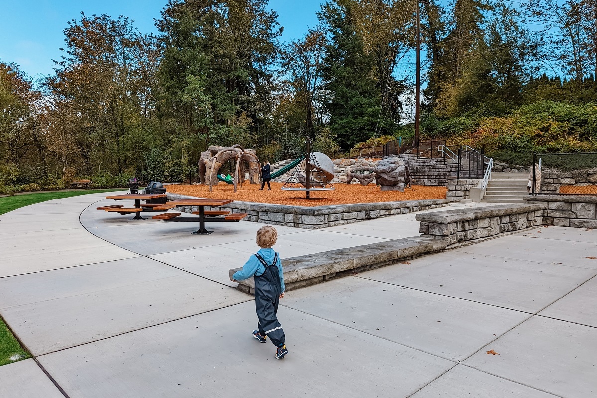 A young boy in a rain suit approaches the new sculptural-looking play equipment at Bellevue’s Newport Hills Woodlawn Park near Seattle
