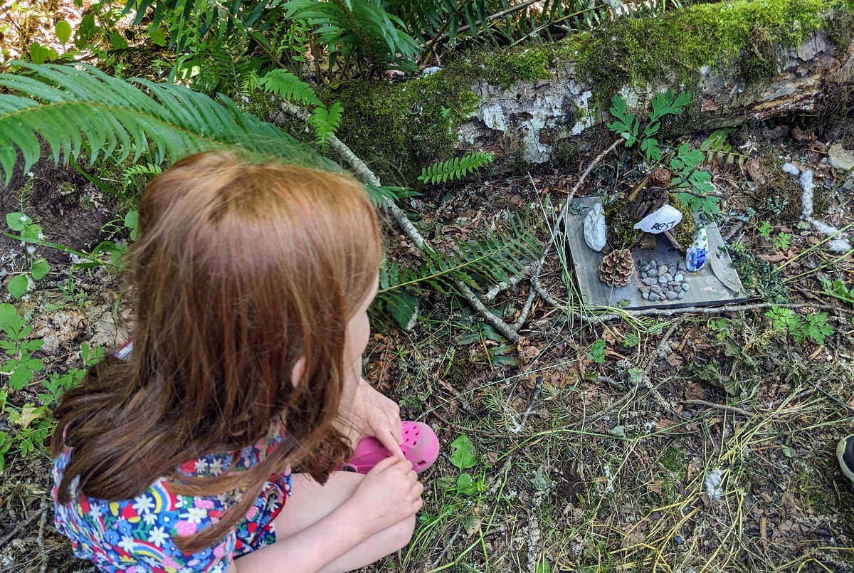 A young girl crouches along the fairy house trail to look more closely at one of the sweet fairy homes in Beaver Lake Preserve