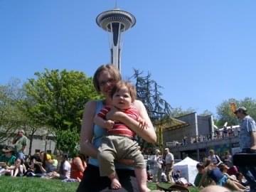 "Mom and baby on the lawn at the Seattle Center with the space needle behind them"