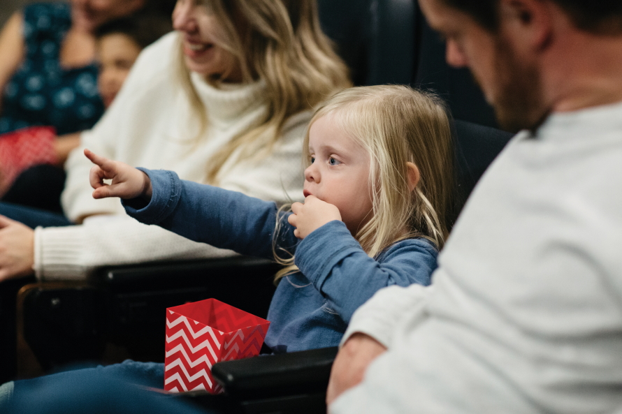 "Young girl pointing and eating popcorn in a movie theater"