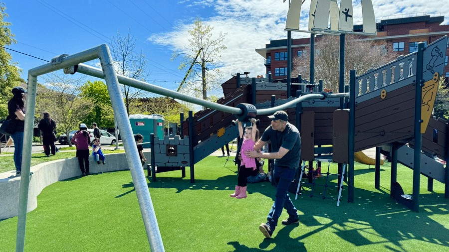 Man helps young daughter across the zipline at the new Ballard Commons Park playground.