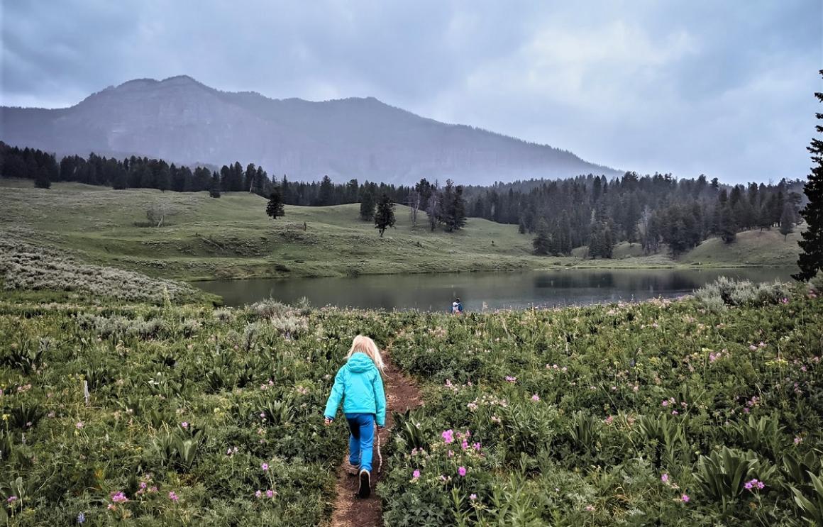 Young girl in bright blue jacket hiking amid beautiful scenery on a stop during a family camper van road trip to western national parks