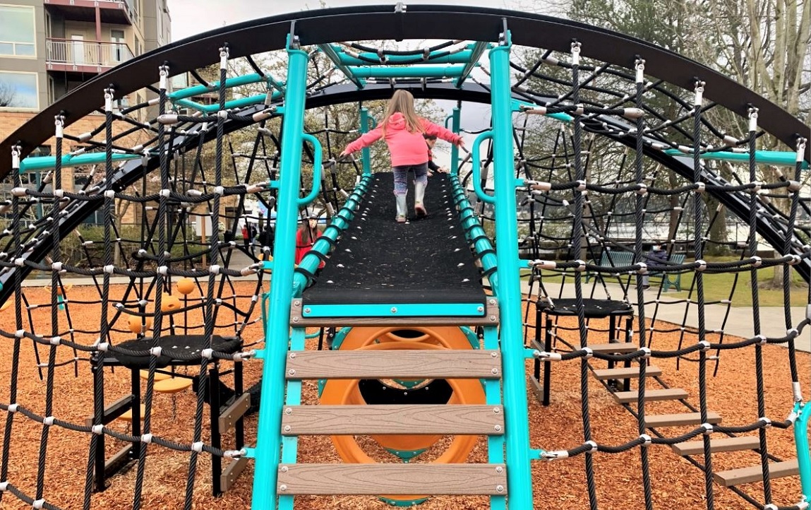 Young girl in pink jacket on large rope climber at new Gene Coulon Memorial Beach Park playground in Renton near Seattle Washington