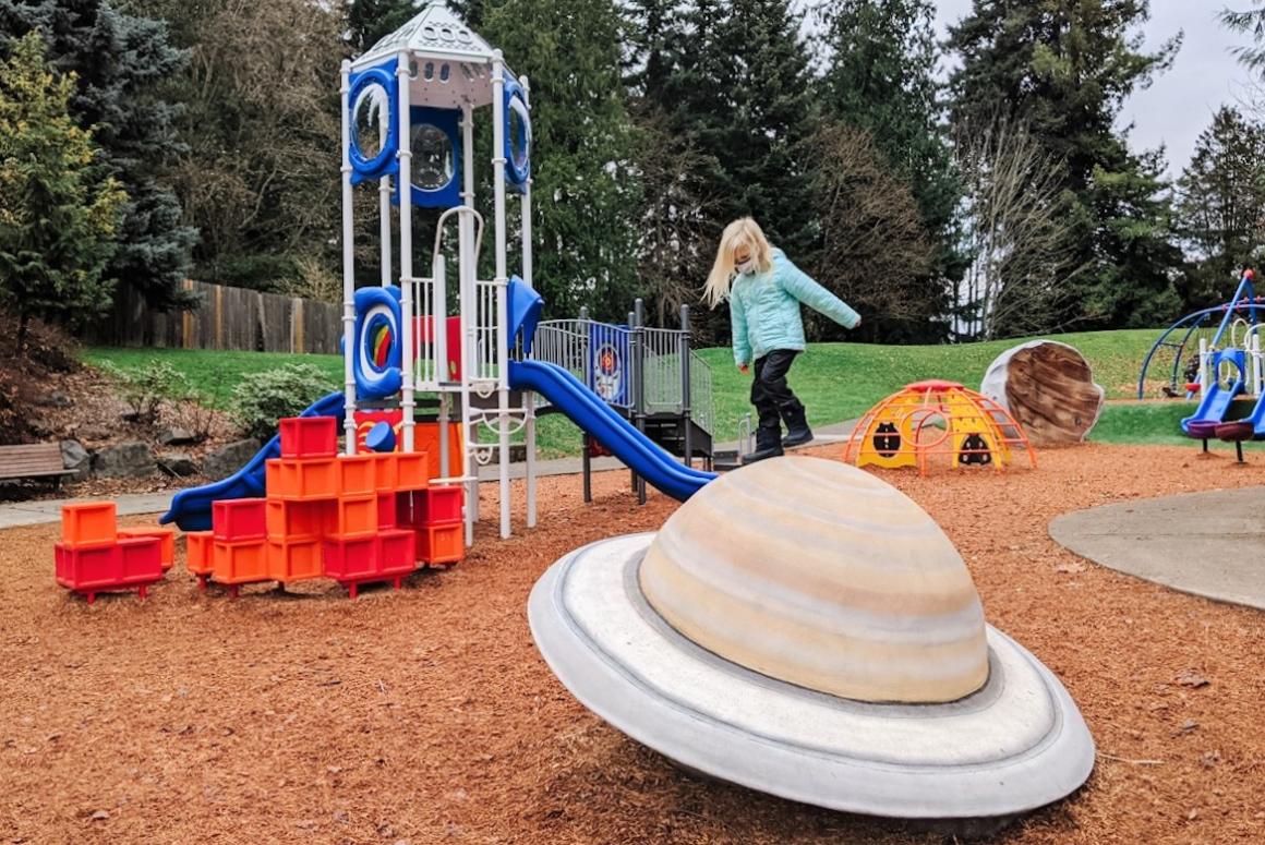 Girl climbing on planet play toy at new space-themed North Kirkland Community Center and Park playground