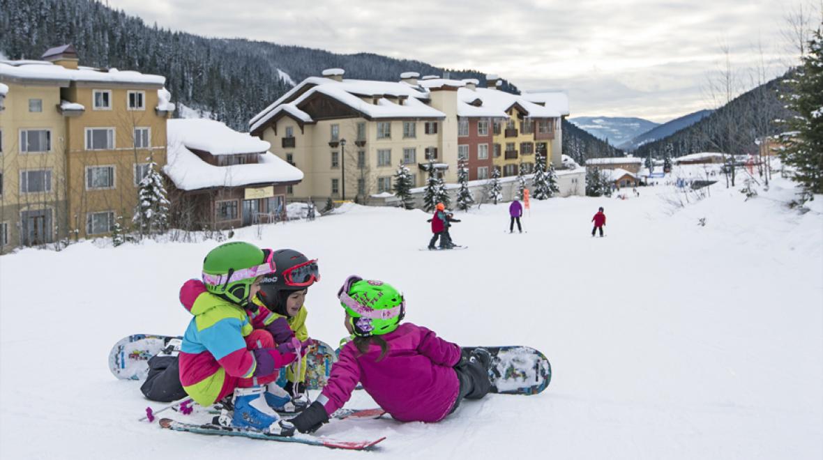 kids sitting on a snowy hill overlooking the resort