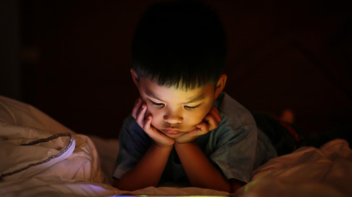 boy watching virtual story time on a tablet in bed