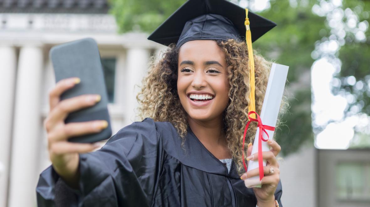 girl in a cap and gown taking a selfie at graduation 2023