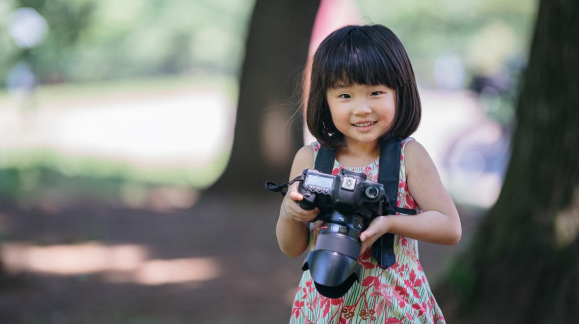 little girl outdoors holding a professional camera