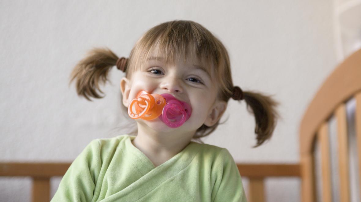 silly girl with two pacifiers in her mouth smiling