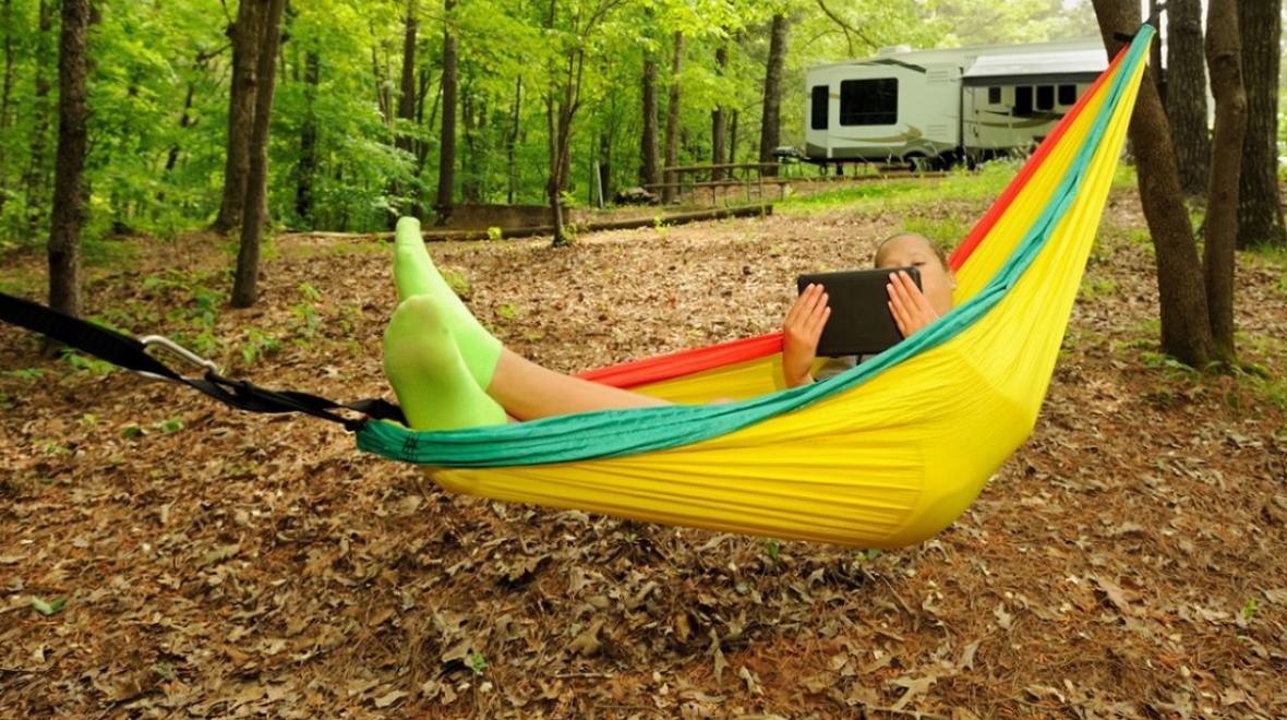 girl reading tablet in yello hammock while camping trailer in the background