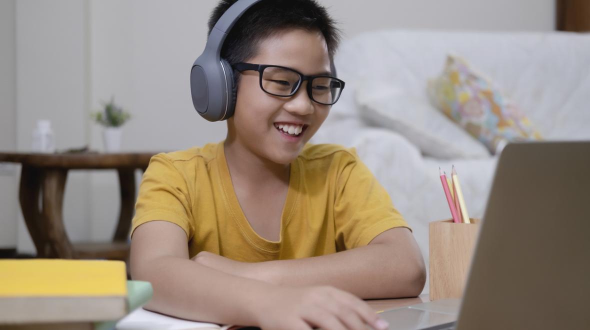 elementary school age boy sitting in front of a laptop smiling