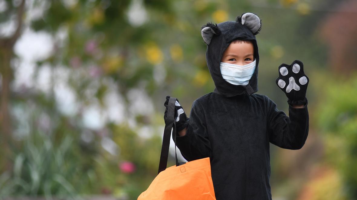 boy wearing a cat costume and mask waving at the camera outdoors Halloween 2020