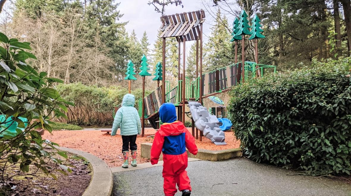 Young kids dressed for rainy weather approaching a new playground at Heron Park in Mill Creek, a small city near Seattle Washington