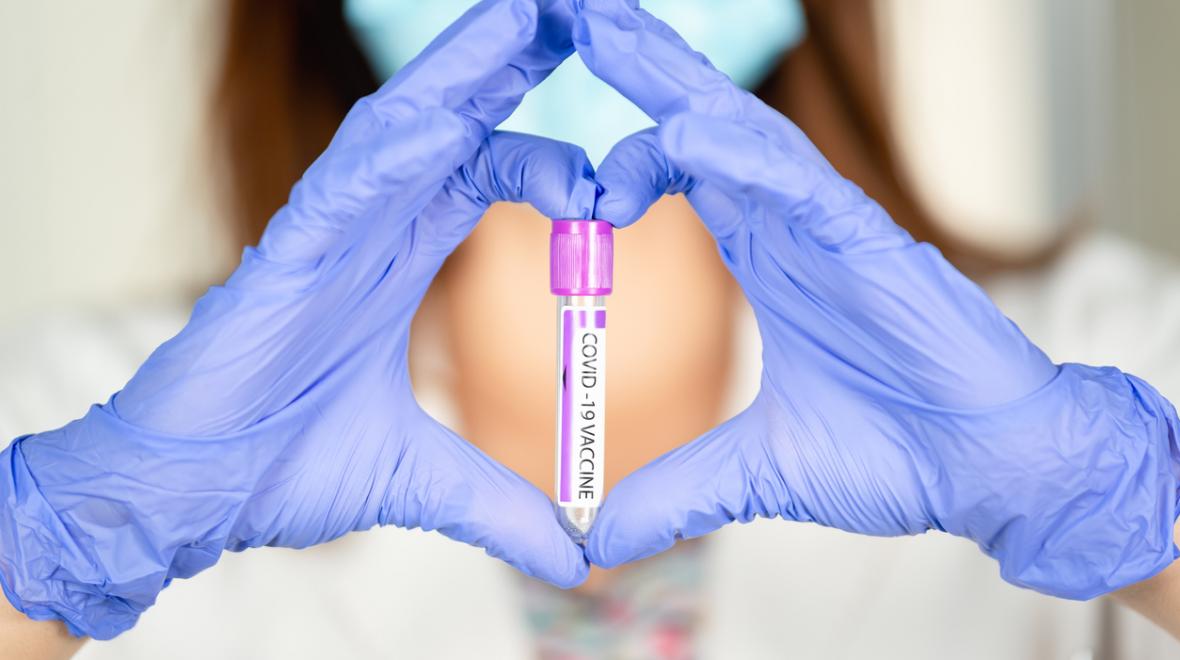 gloved hands making the shape of a heart around a vial with a covid vaccine label