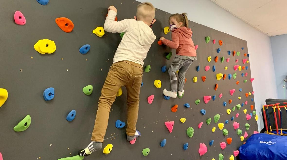 Two young kids wearing masks climb on an indoor climbing wall at Kaleidoscope Family Gym indoor play gym in Puyallup, Wash.