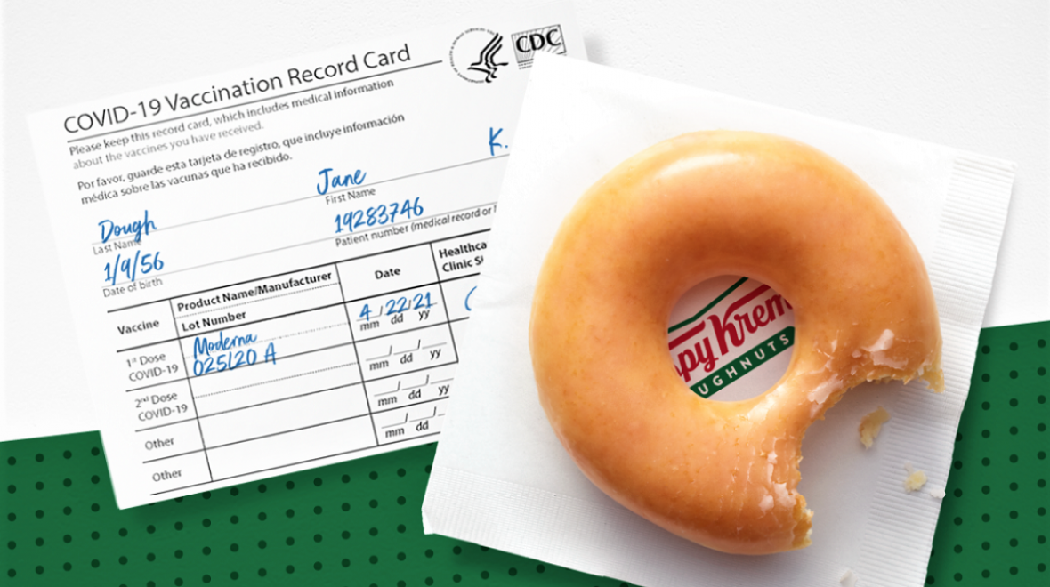 A sample COVID 19 vaccine card alongside a Krispy Kreme glazed doughnut sitting on a napkin; doughnut chain offering free doughnuts to vaccinated individuals