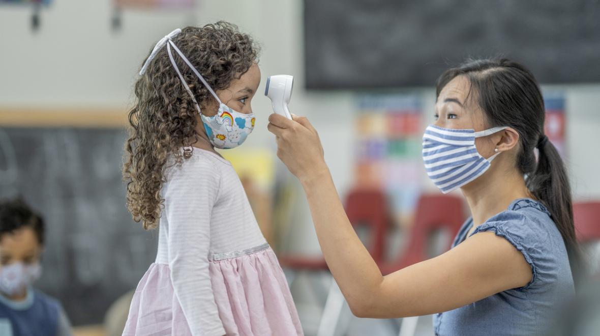 daycare woman in a mask taking a child's temperature