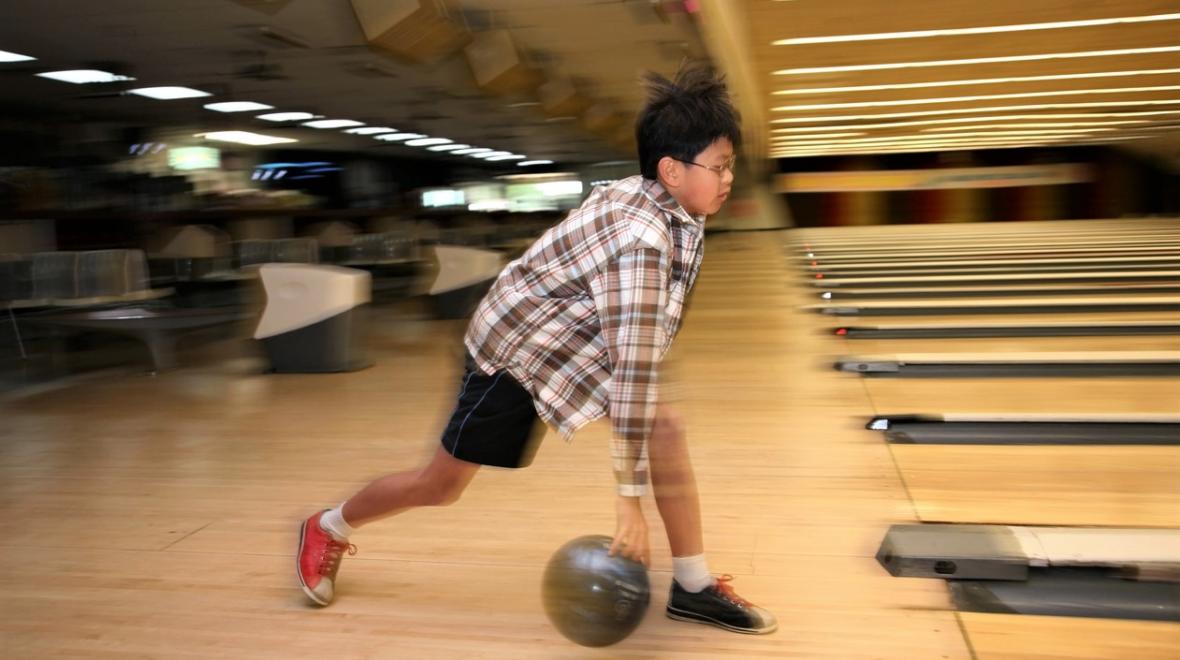 Boy in plaid shirt and short bowling at bowling alley near Seattle Kids Bowl Free program Seattle area kids families