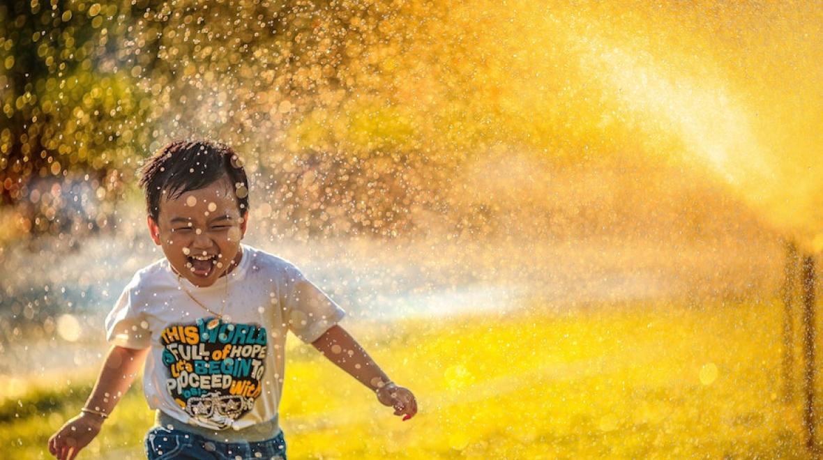 boy running through a sprinkler backlit by the sun