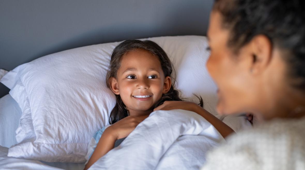 mother sitting on the side of her daughter's bed with both smiling