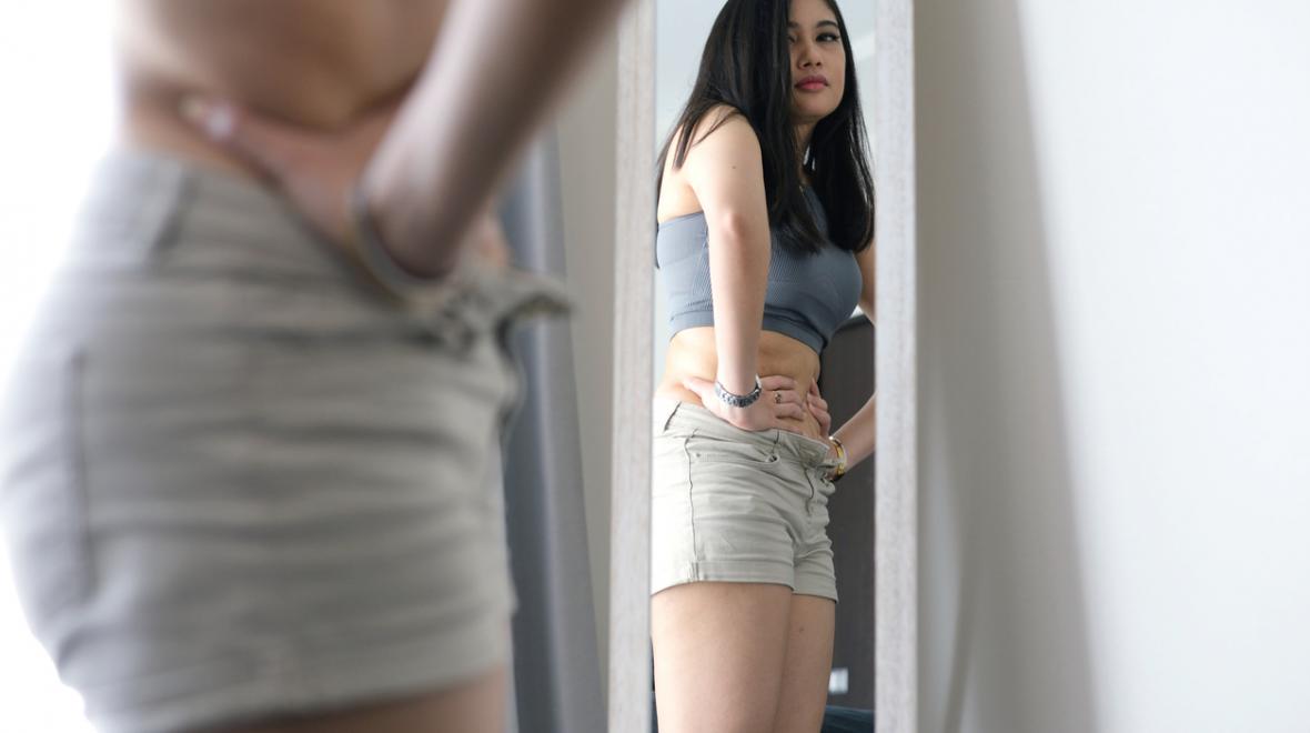 A young woman looking at her reflection in the mirror, unhappy with what she is seeing
