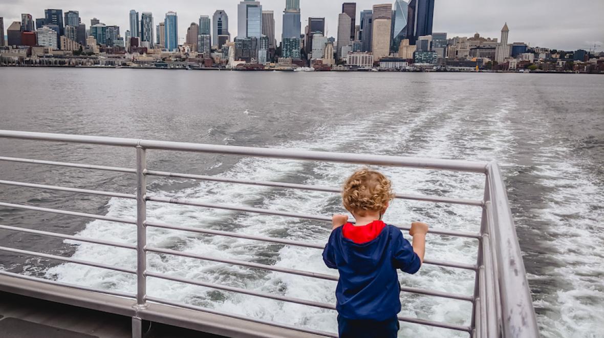 curly-haired blond boy looking at the Seattle skyline from the deck of the west seattle water taxi