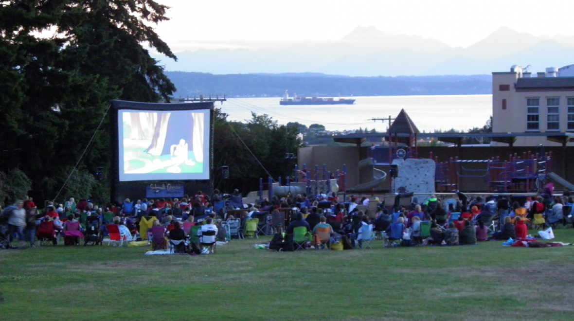 People relax in the grass at a park watching a free outdoor summer movie for kids and families