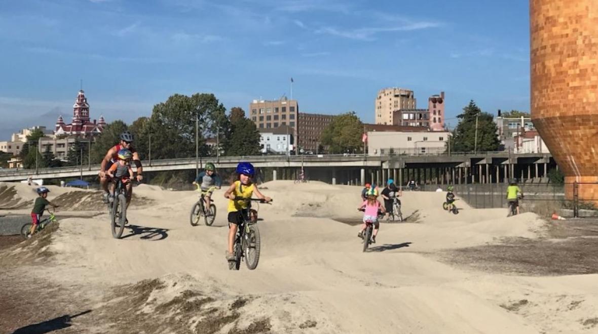 Kids and a dad with a baby on his bike ride on the pump track at Bellingham's Waypoint Park near downtown on the site of the old Georgia Pacific plant