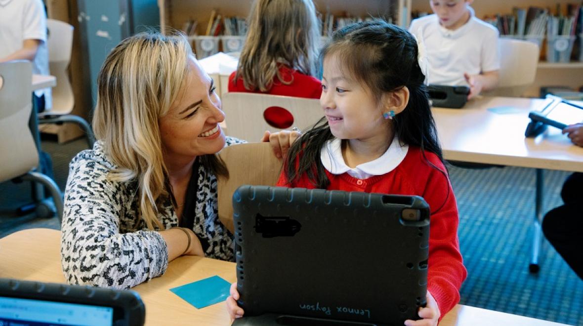 Young student at the Ephiphany school works on a laptop and is helped by her math teacher
