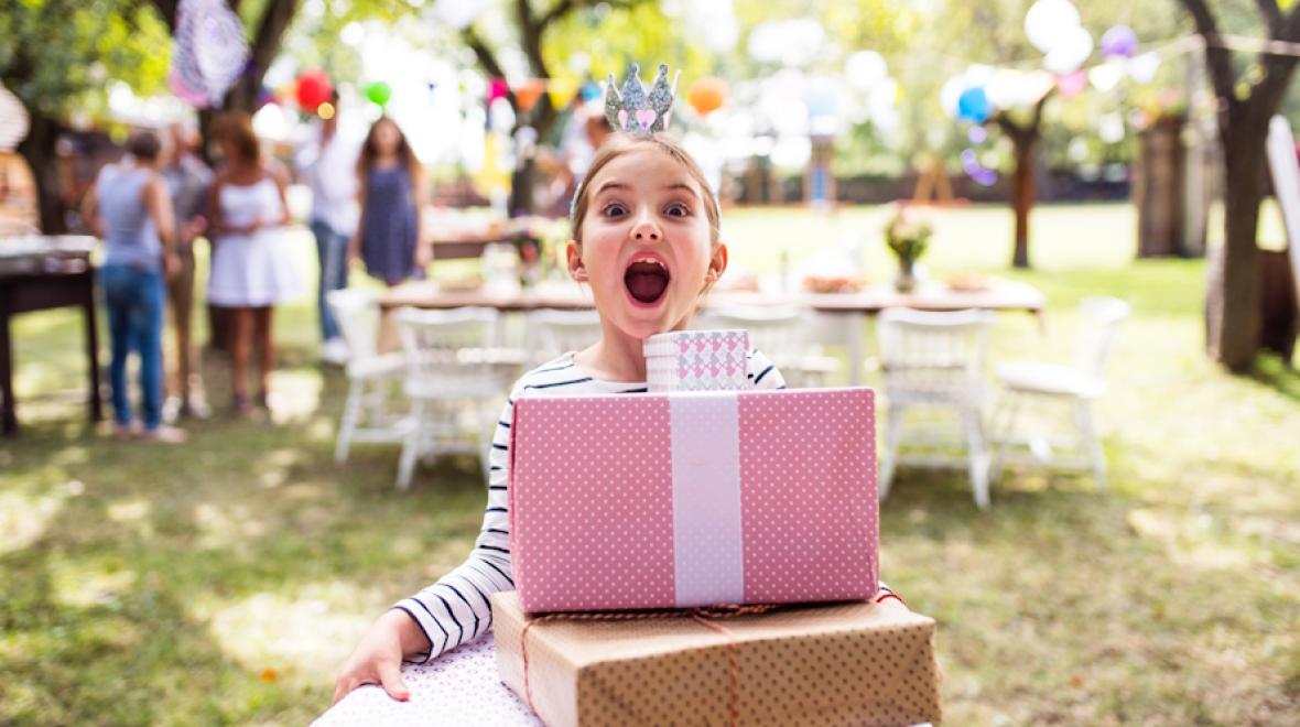 Young girl holding a stack of packages at a birthday party in a park