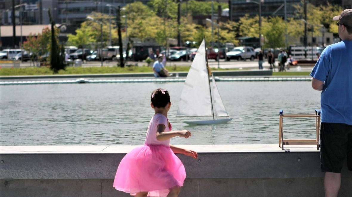 A girl in a pink skirt sails a pond boat on the pond at Lake Union Park among best summer activities in Seattle