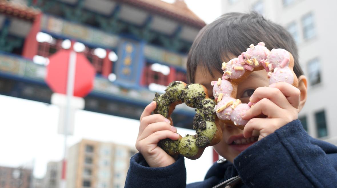 A boy holds two Dochi doughnuts over his eyes; eating doughnuts is among the best fall activities in Seattle