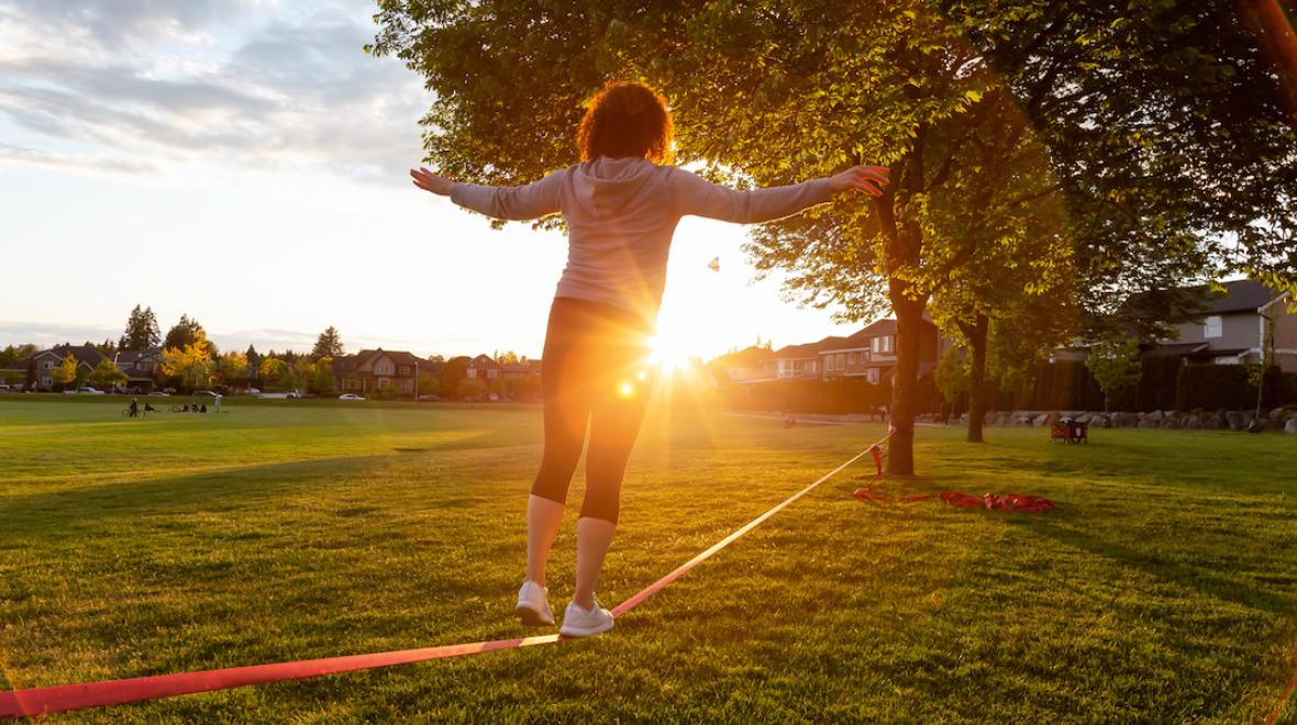 Back view of a person walking on a slackline with the sun setting.