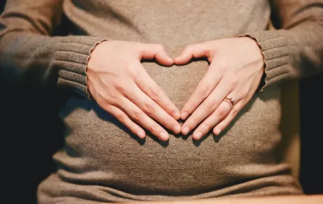 woman making heart shape on pregnant belly