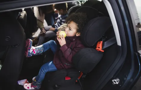 little boy eating an apple in the back seat of a car is an easy road trip snack for kids that is healthy