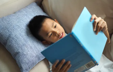 little boy lying on his back on the couch reading