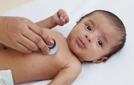 hand holding a stethoscope to a baby's bare chest