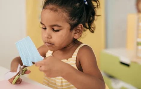 little girl cutting colorful construction paper with scissors 