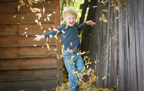 boy dancing in gold tumbling leaves with wooden buildings in the background