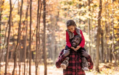 father with daughter on his shoulders surrounded by trees with fall colors