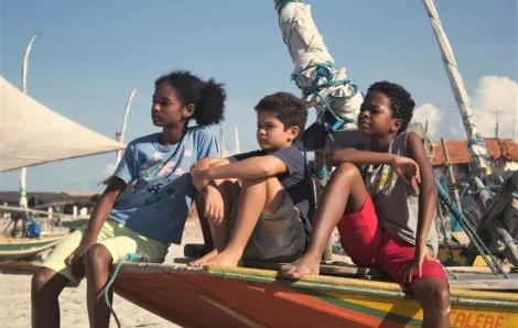 young warriors childrens film festival still image of three kids sitting on the prow of a small boat on the beach